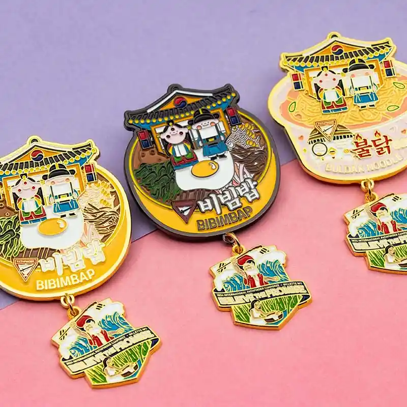 Three colorful Korean-themed custom enamel medals featuring cartoon characters and food designs, each with a dangling charm, displayed on a pastel background.