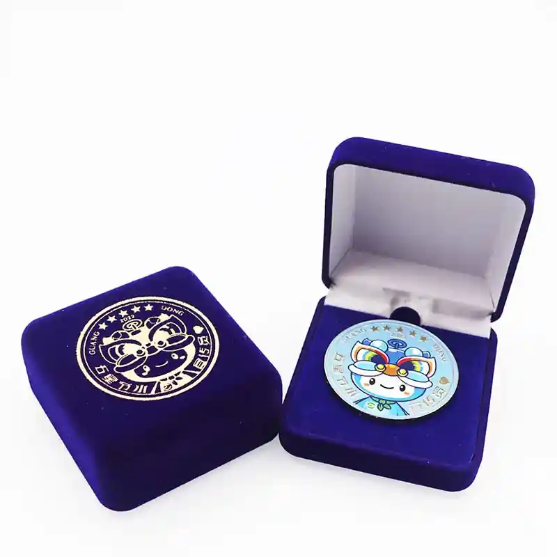 A colorful custom souvenir enamel coin displayed inside a blue velvet gift box, with another closed velvet box placed beside it.