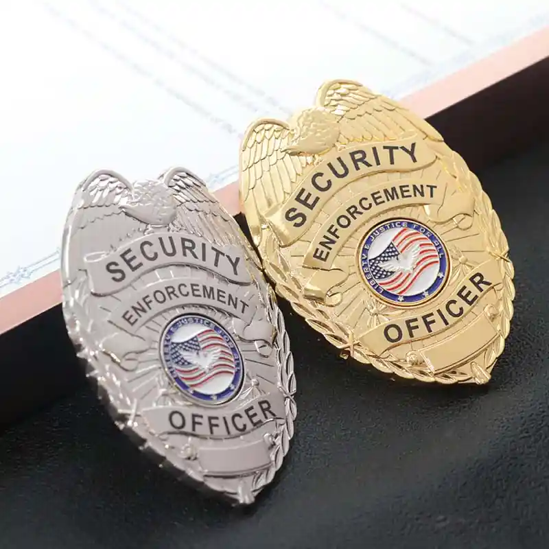 Two custom security officer badges in gold and silver finishes, featuring an eagle emblem and American flag center seal, displayed on a desk surface.