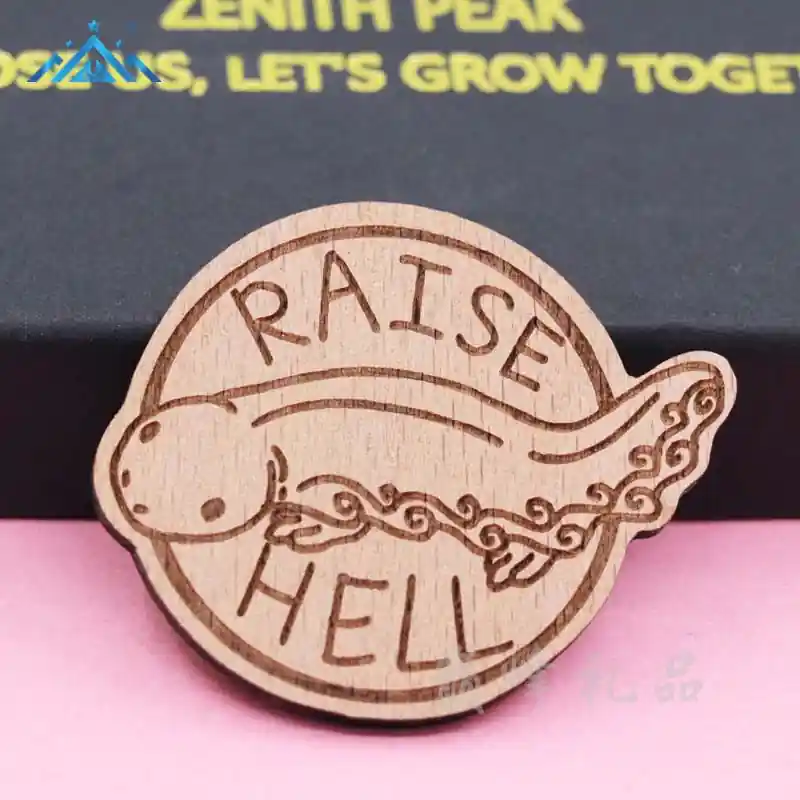 A custom wooden pin featuring a cute axolotl design with laser engraved text “Raise Hell,” displayed against a pink background with packaging behind it.