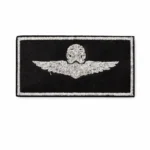 A rectangular embroidered patch featuring a winged emblem in silver on a black background. The patch has no backing material visible, providing a clean edge.
