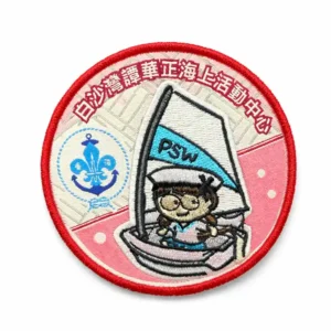 A round embroidered scout patch with a red border, featuring a cartoon scout sailing a small boat with a flag marked “PSW,” Chinese text around the top edge, and a scout emblem on the left against a pink and cream background.