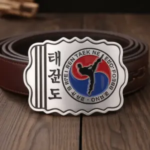 A metal belt buckle featuring Korean characters and a taekwondo kicking silhouette inside a red and blue taegeuk symbol.