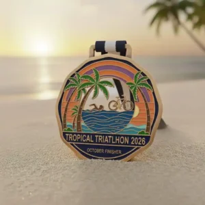 Custom metal triathlon medal featuring swimming, cycling, and running icons with tropical sunset and palm trees, Tropical Triathlon 2026 medal with blue and white ribbon on sandy beach background