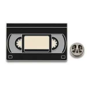 Black VHS tape enamel badge with blank cream label, gray reels, silver dividers, and butterfly clutch.