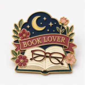 Glasses moon Book Lover enamel pin with gold metal outline, open book, red glasses, moon and stars, floral accents, burgundy Book Lover banner, and cream background on a white surface.