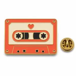 Heart mixtape enamel badge with coral cassette shell, blank label, cream reels, gold dividers, and butterfly clutch.