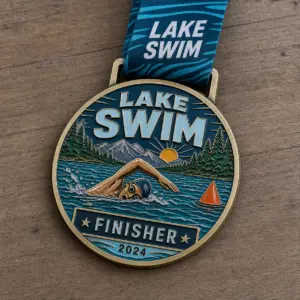 Mountain lake finisher Lake Swim Medal soft enamel medal with raised gold outlines, swimmer, blue lake waves, pine forest, mountain view, buoy, and ribbon.