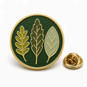 Round botanical leaf enamel badge with three green leaves, gold metal dividers, and butterfly clutch.