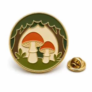 Round soft enamel mushroom forest badge with two red mushrooms, green trees, gold metal outline, and butterfly clutch on white background.