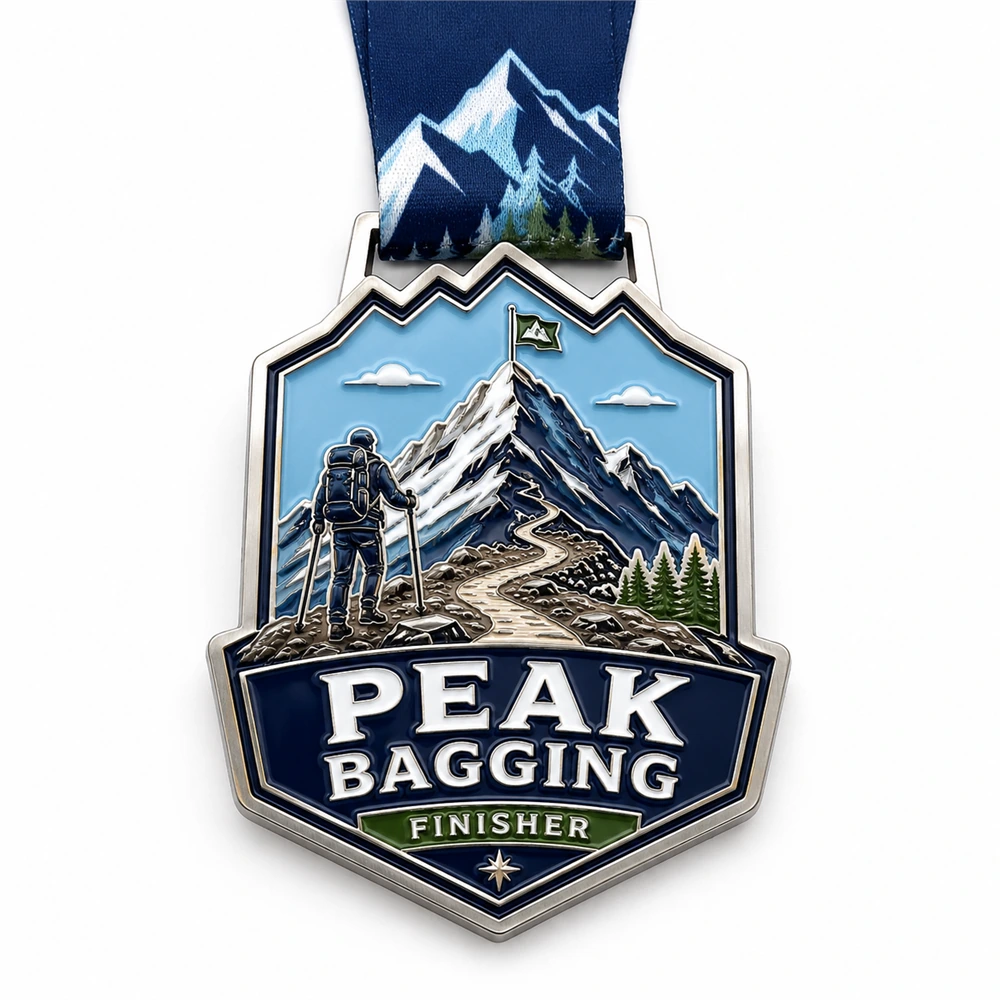 Detailed mountain hiker Peak Bagging Medal soft enamel medal with raised silver outlines, backpack hiker, snowy peak, winding summit trail, pine trees, ribbon loop, and mountain neck ribbon on a white background.