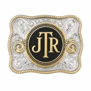 Hebilla de cinturón negra con el monograma JTR, con iniciales doradas, centro circular negro, grabado floral plateado, detalles dorados en forma de voluta, borde dorado tipo trenza y fondo blanco.