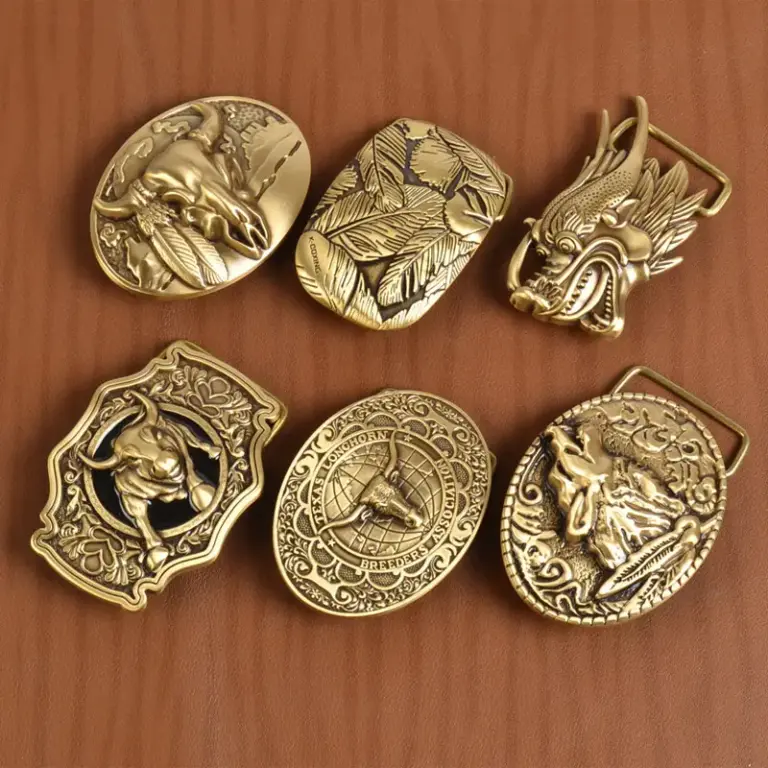 A collection of brass belt buckles displayed on a brown leather surface, featuring western-style engraved designs including bull skulls, leaves, dragon head, longhorn, and animal motifs.