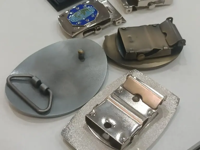 A display of custom belt buckle components showing different buckle backs, clips, attachments, and metal hardware parts for belt buckle manufacturing.