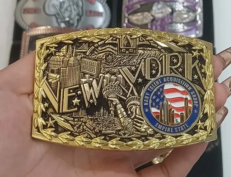 A custom zinc alloy belt buckle featuring a detailed New York city design, gold finish, raised lettering, laurel border, and colorful enamel emblem.