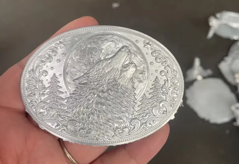 A silver metal belt buckle blank after die casting, featuring a detailed embossed wolf design with decorative border patterns before finishing and plating.